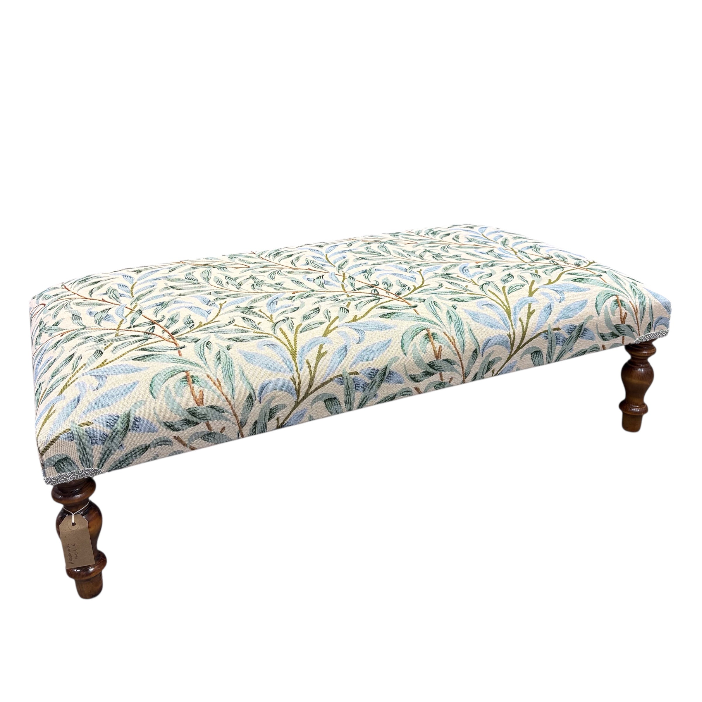 A beautiful hand crafted footstool or coffee table covered in William Morris Willow Bough embroidery fabric. The fabric features pale green and blue leaves on a cream background. &nbsp;The footstool has turned mahogany stained legs and is available in store now.