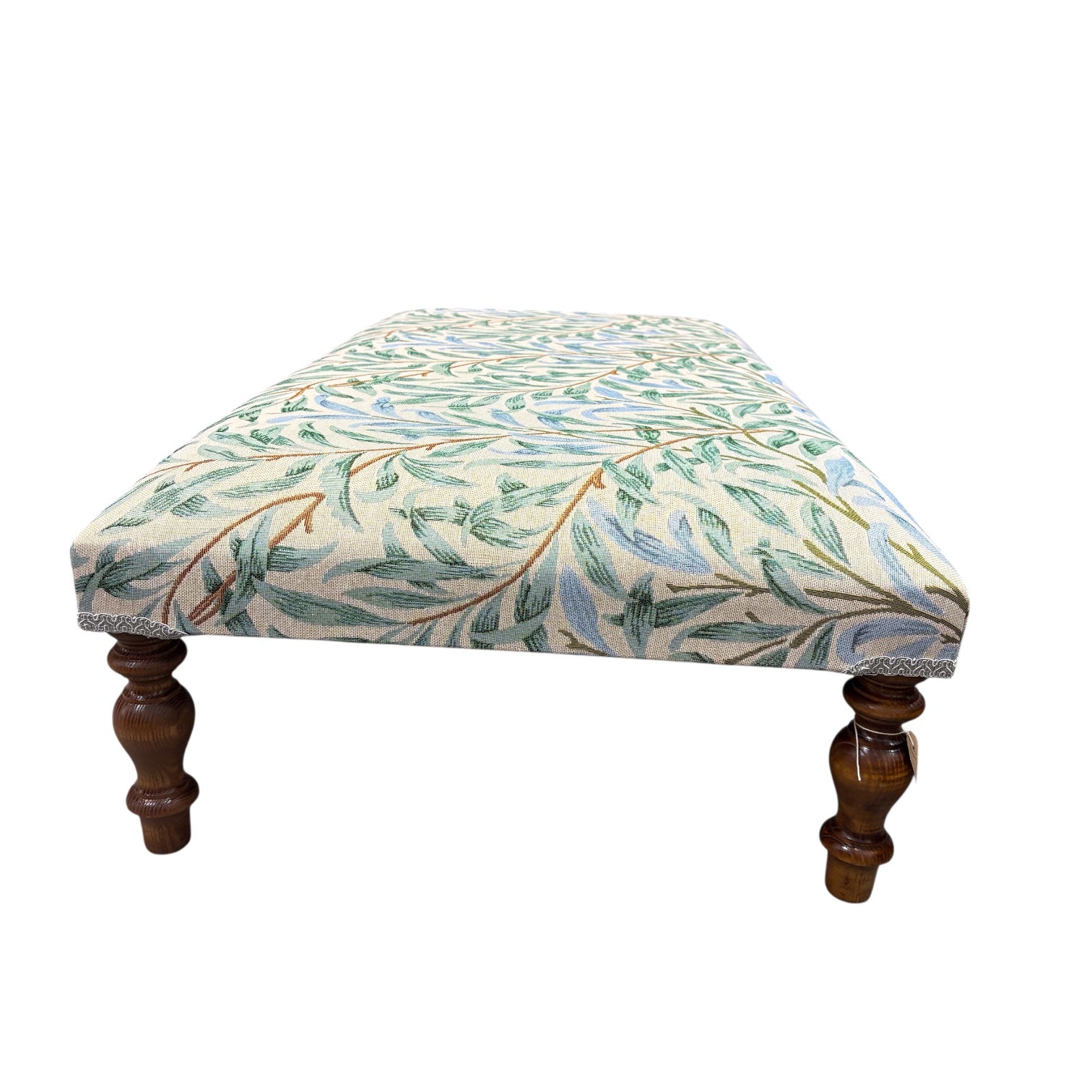 A beautiful hand crafted footstool or coffee table covered in William Morris Willow Bough embroidery fabric. The fabric features pale green and blue leaves on a cream background. &nbsp;The footstool has turned mahogany stained legs and is available in store now.