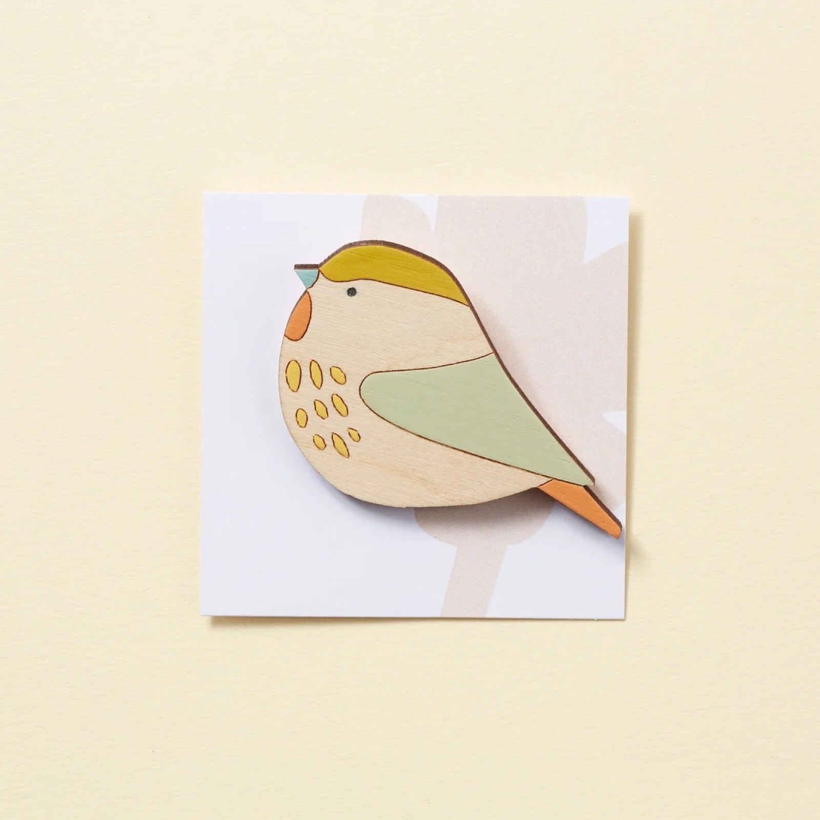 Wooden bird brooch on a white card with a yellow background.
