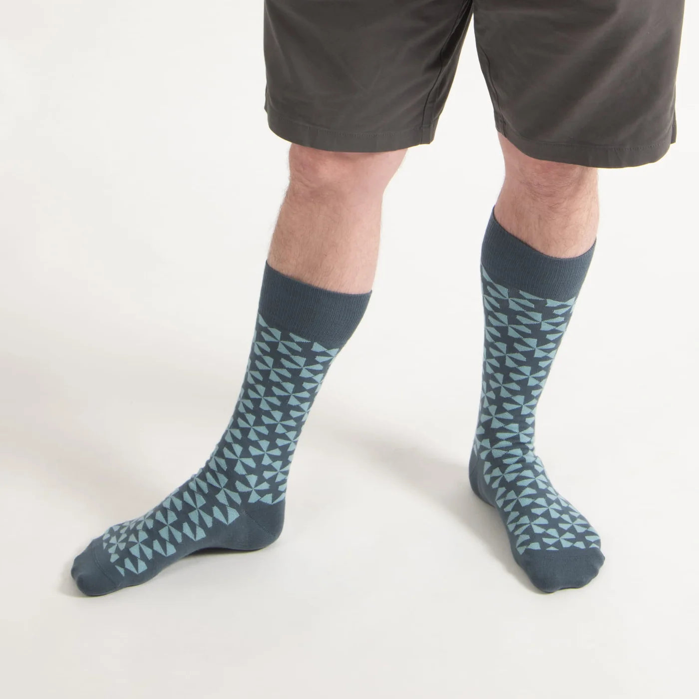 Man wearing blue geometric socks and shorts, in a white room.