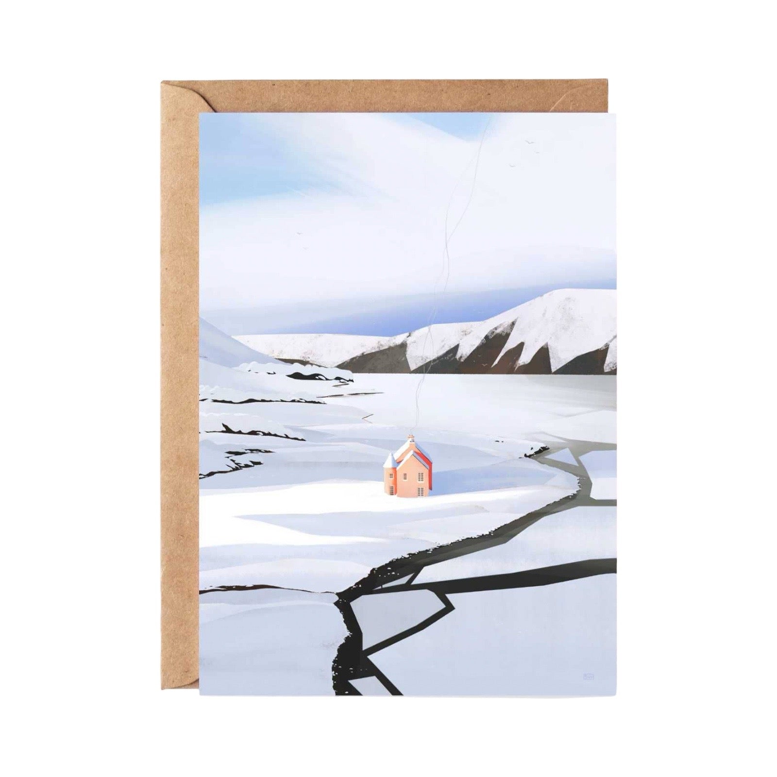 A greeting card featuring a snowy landscape with a small pink house, shown with a brown kraft envelope behind it on a white background.