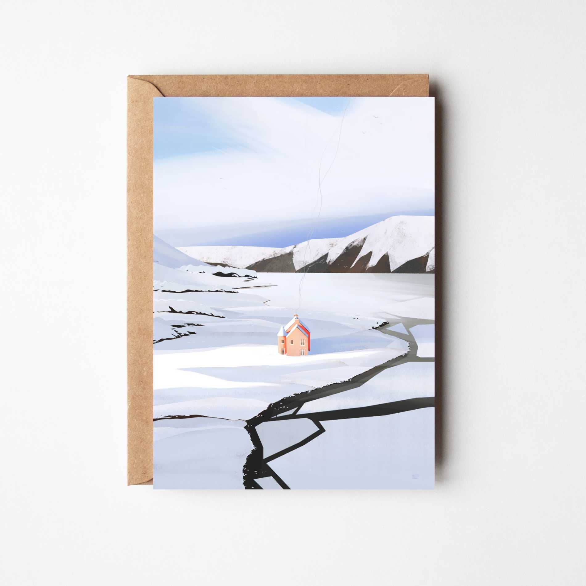 A greeting card with a kraft paper envelope, featuring an illustration of a snowy landscape with a small pink house and dark cracked ground, displayed against a light grey background.