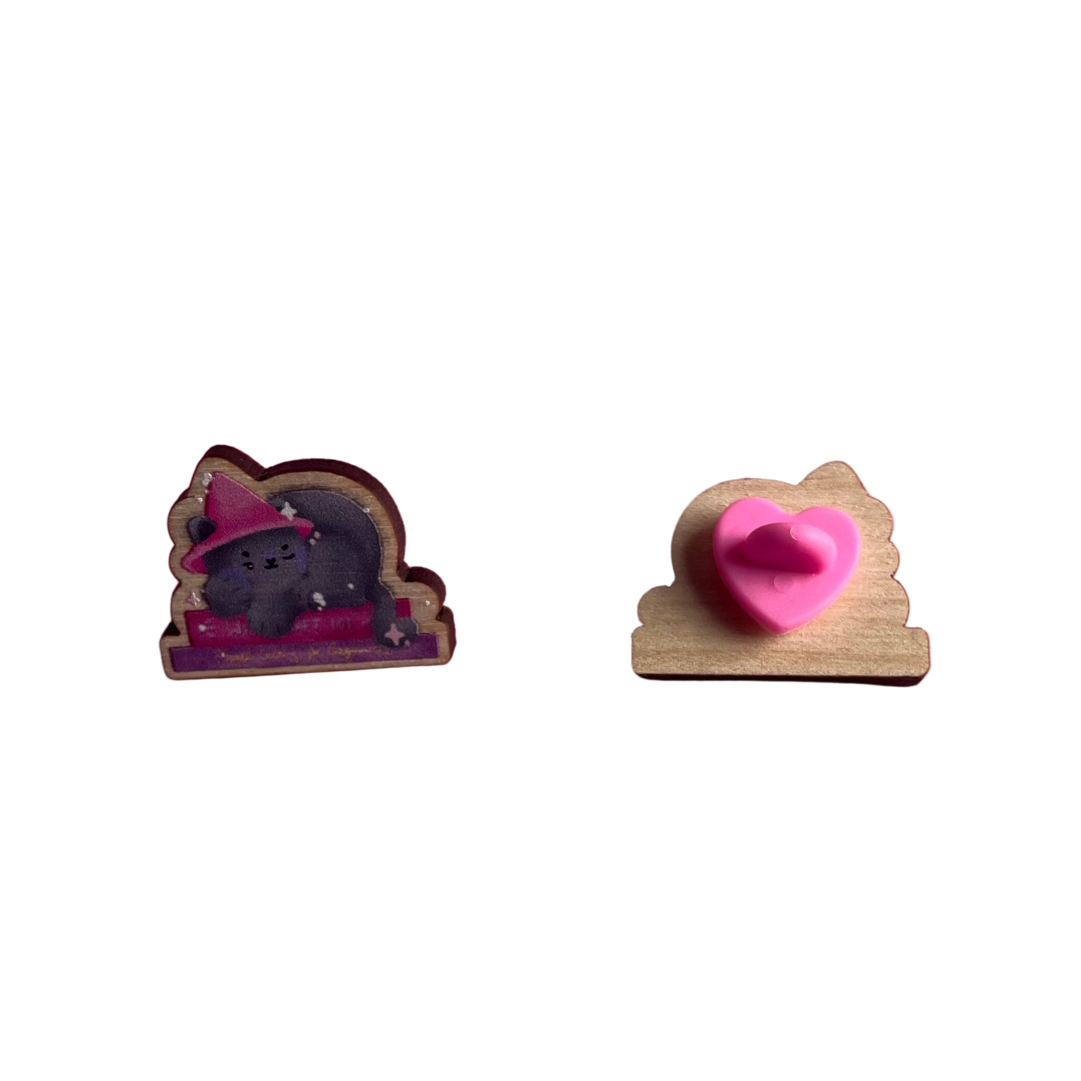 Wooden pin badge of a grey cat wearing a pink witch's hat, sleeping on a stack of books. Book titles are 'Witchcraft 101' and 'Spellcasting for Beginners'. This badge is printed onto 3mm thick responsibly sourced European birch plywood.