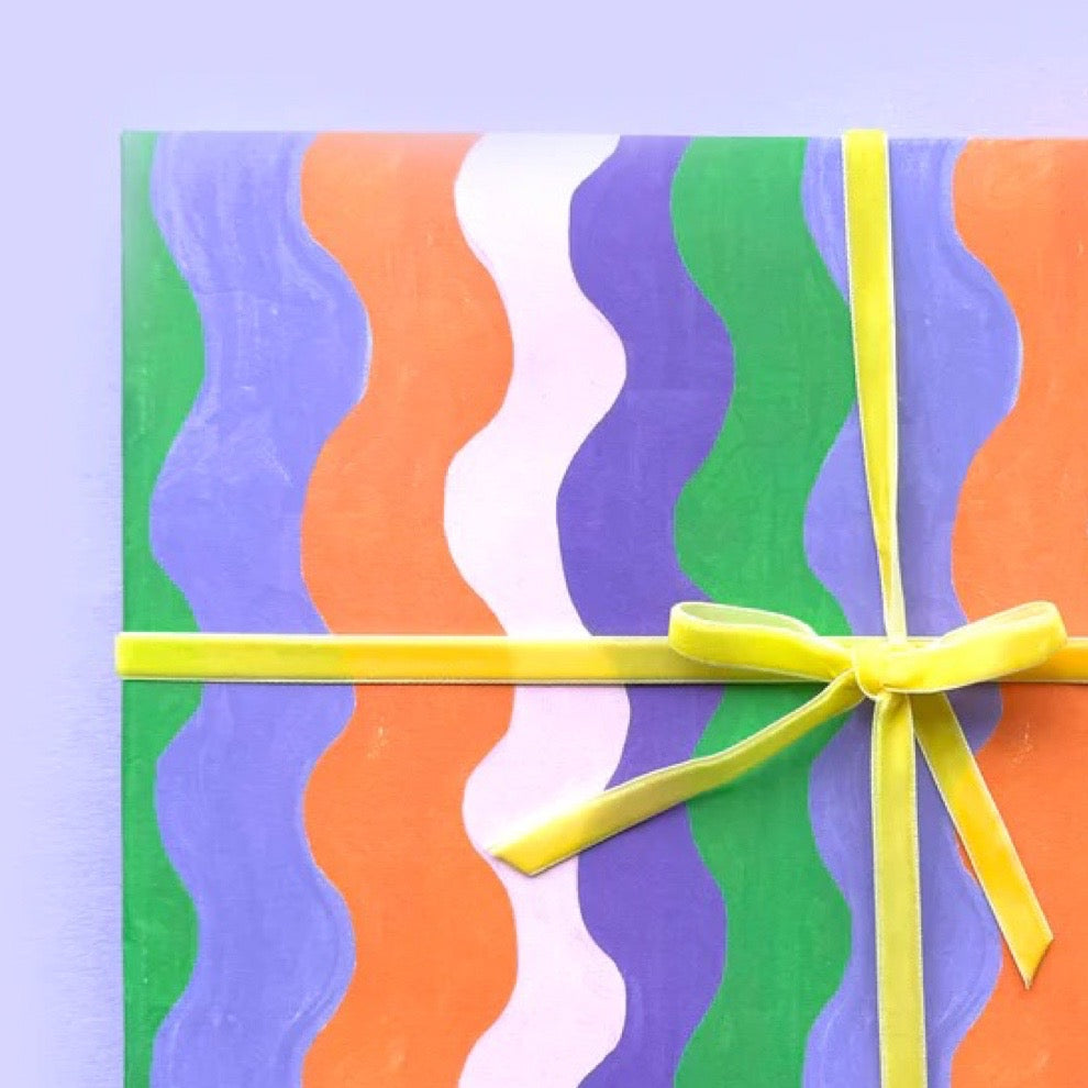 Colourful gift with wavy patterns and a yellow ribbon on a light purple background.