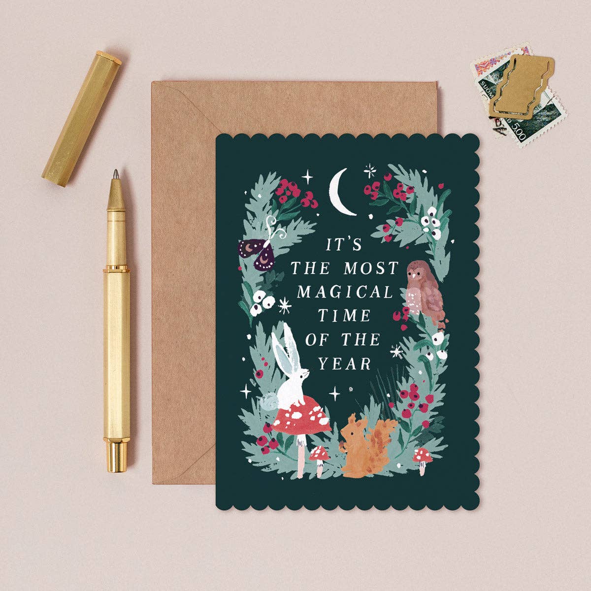 Greeting card with floral design and text, envelope, and pen on a beige background with a pen and stamps.