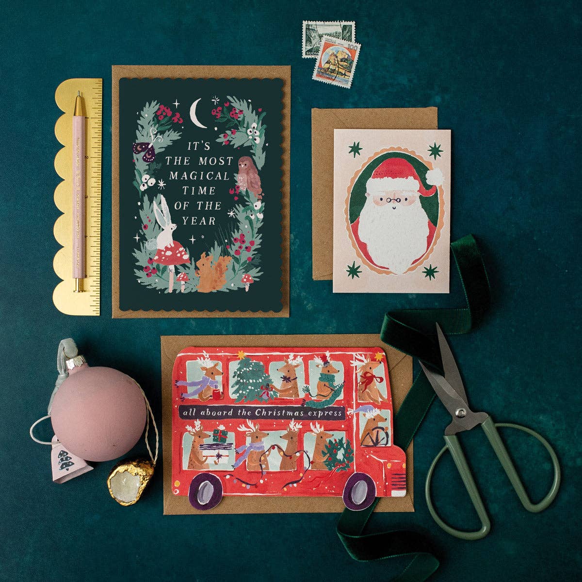 Collection of Christmas-themed cards and decorations on a dark green surface with scissors and other items.