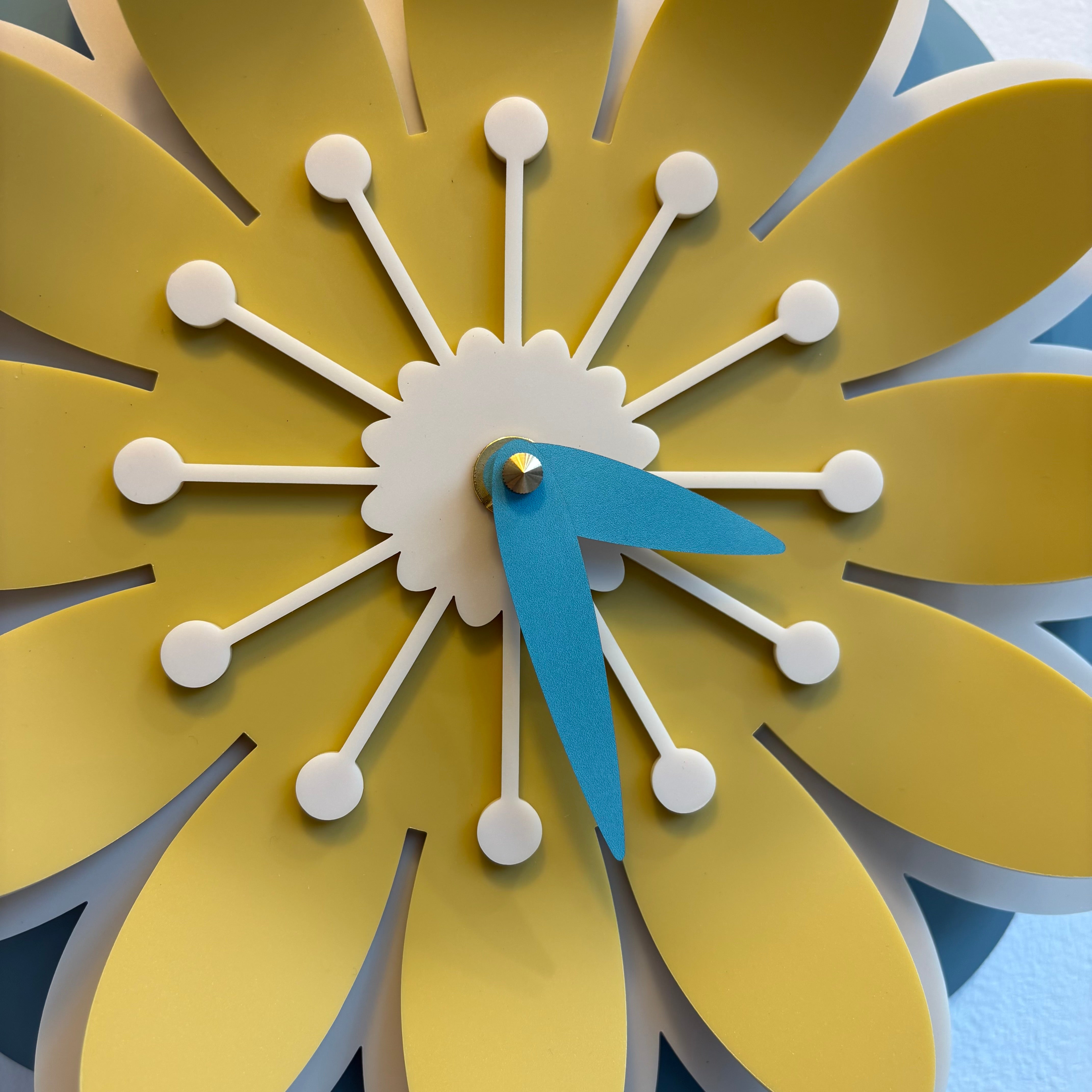 Decorative wall clock designed like a yellow flower with blue hands.