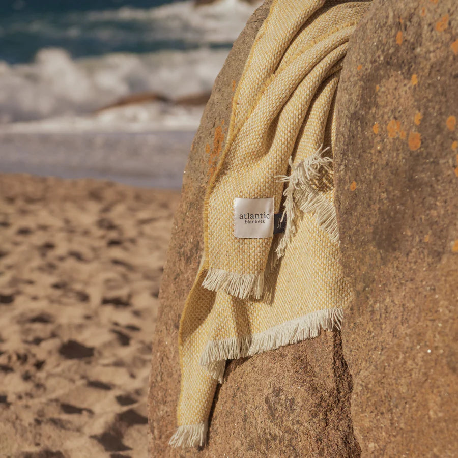 Yellow blanket with a brand tag draped over a rock on the beach.