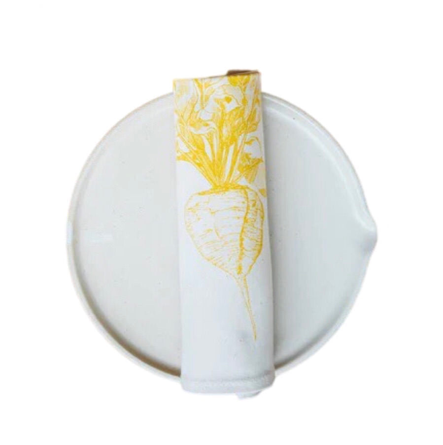Cream cotton napkin with a yellow sugar beet rolled on a plate.