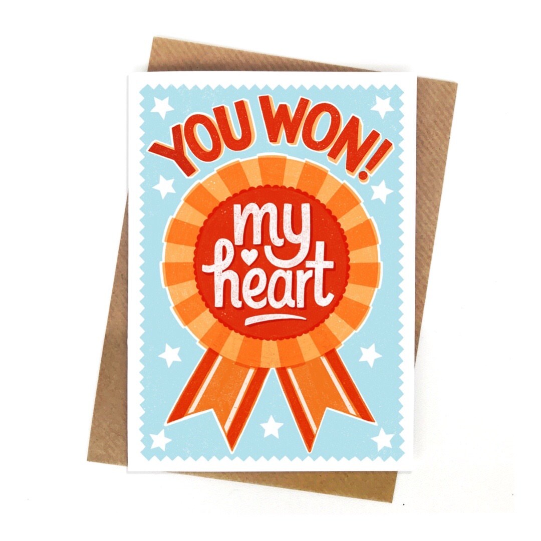 A card featuring a red and orange rosette in the centre with the text 'you won my heart', all on a pale blue background with a white border.