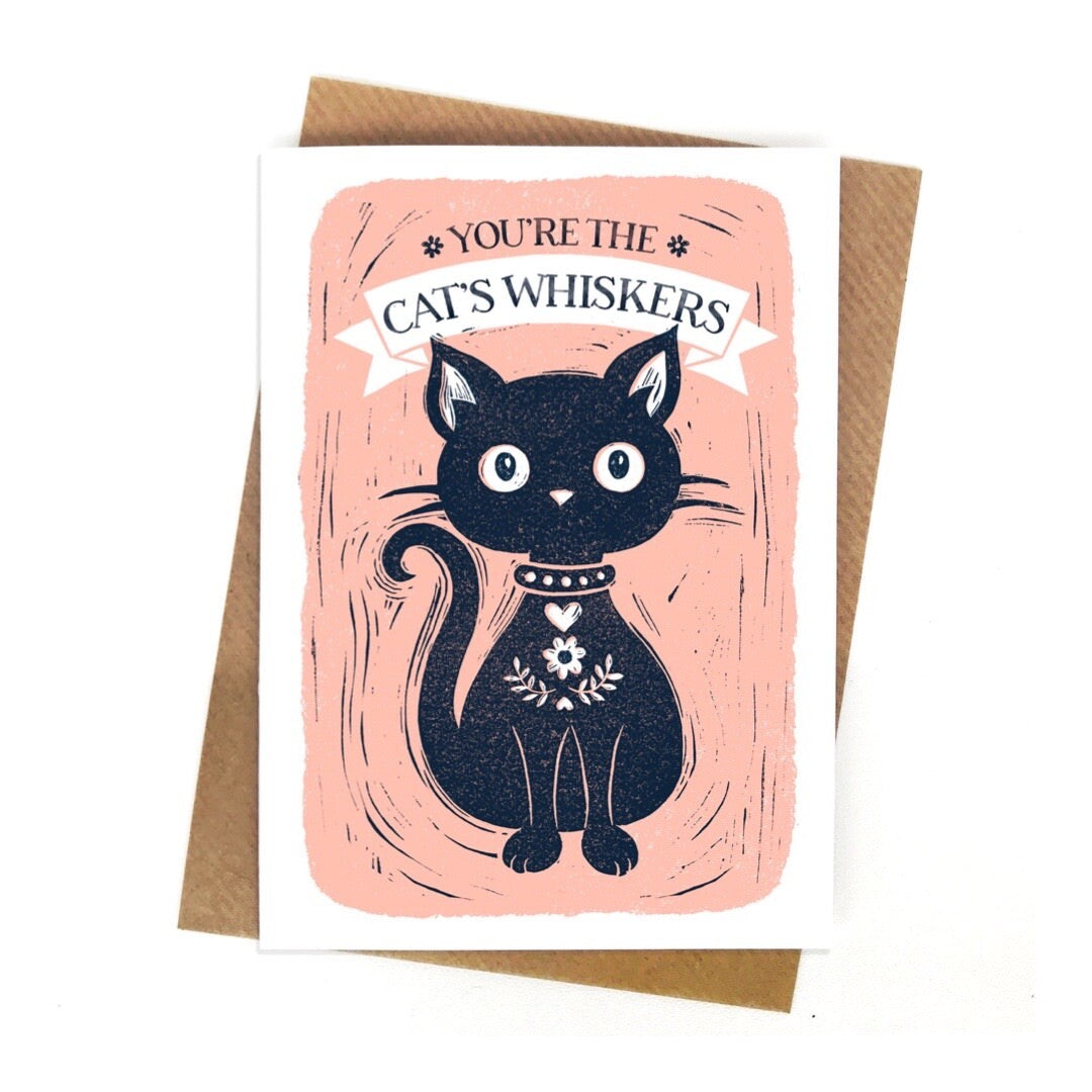 A card with a beautiful black cat with large eyes and a diamond collar and the text you're the cats whiskers written above, all on a pale pink background with a white border.