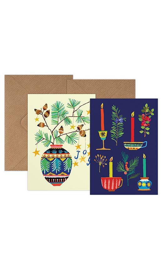 A holiday greeting card set featuring a cream card with a colourful patterned vase, pine branches, butterflies, and 'Joy' text, alongside a dark navy card with candles, botanical motifs, and holiday vessels, both shown with brown kraft envelopes on a white background.